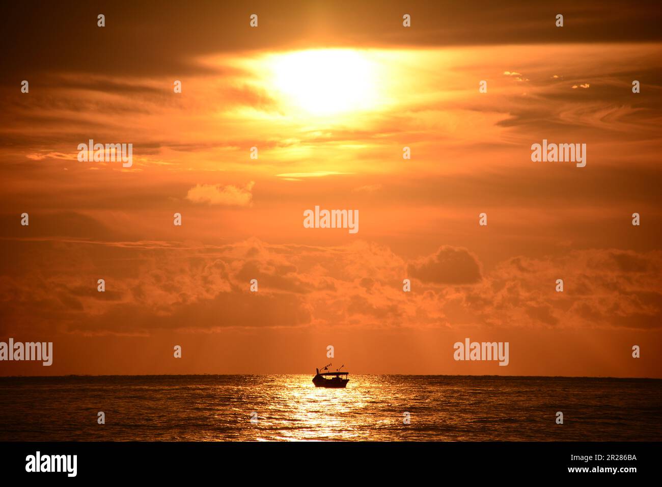Sunset Over the Ocean with Boat Silhouette. The vibrant hues of the setting sun paint the sky in a symphony of warm colors Stock Photo