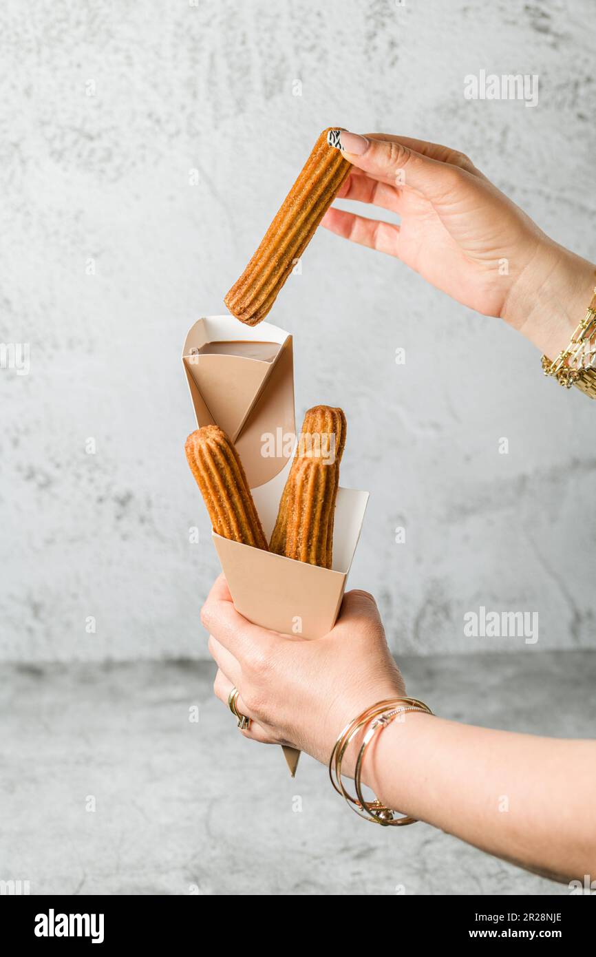 Woman taking churros from a cone and dipping it in chocolate sauce Stock Photo