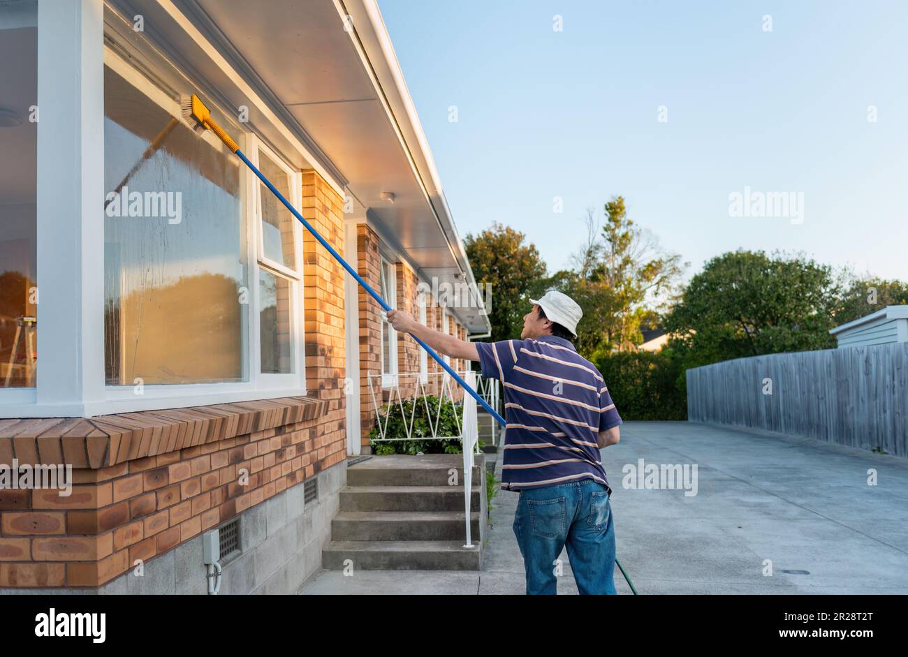 Man washing windows with long pole and brush. Home maintenance. Auckland. Stock Photo