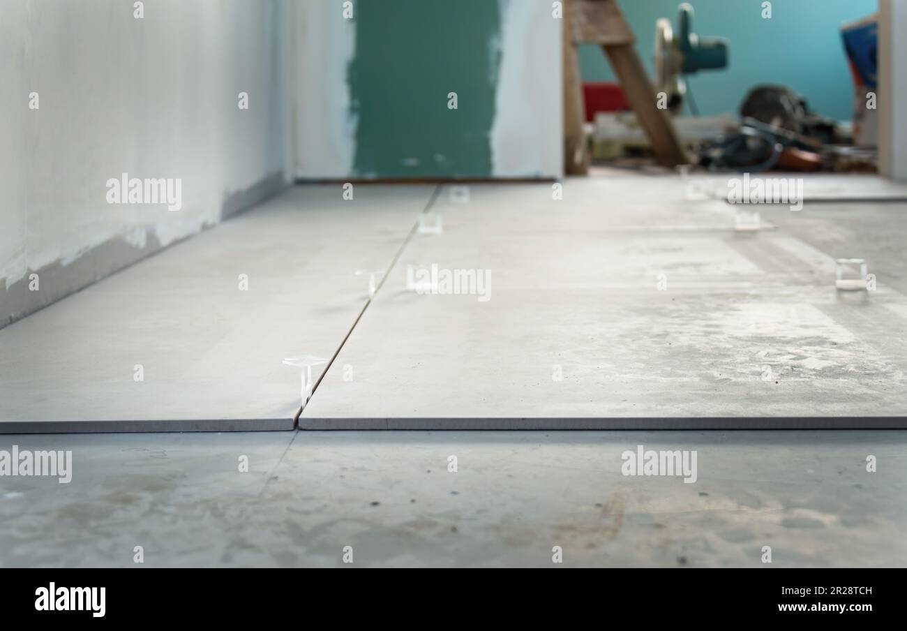 Kitchen floor tiles with levelling wedges and spacers before grouting. Out-of-focus renovation tools in the background. Stock Photo