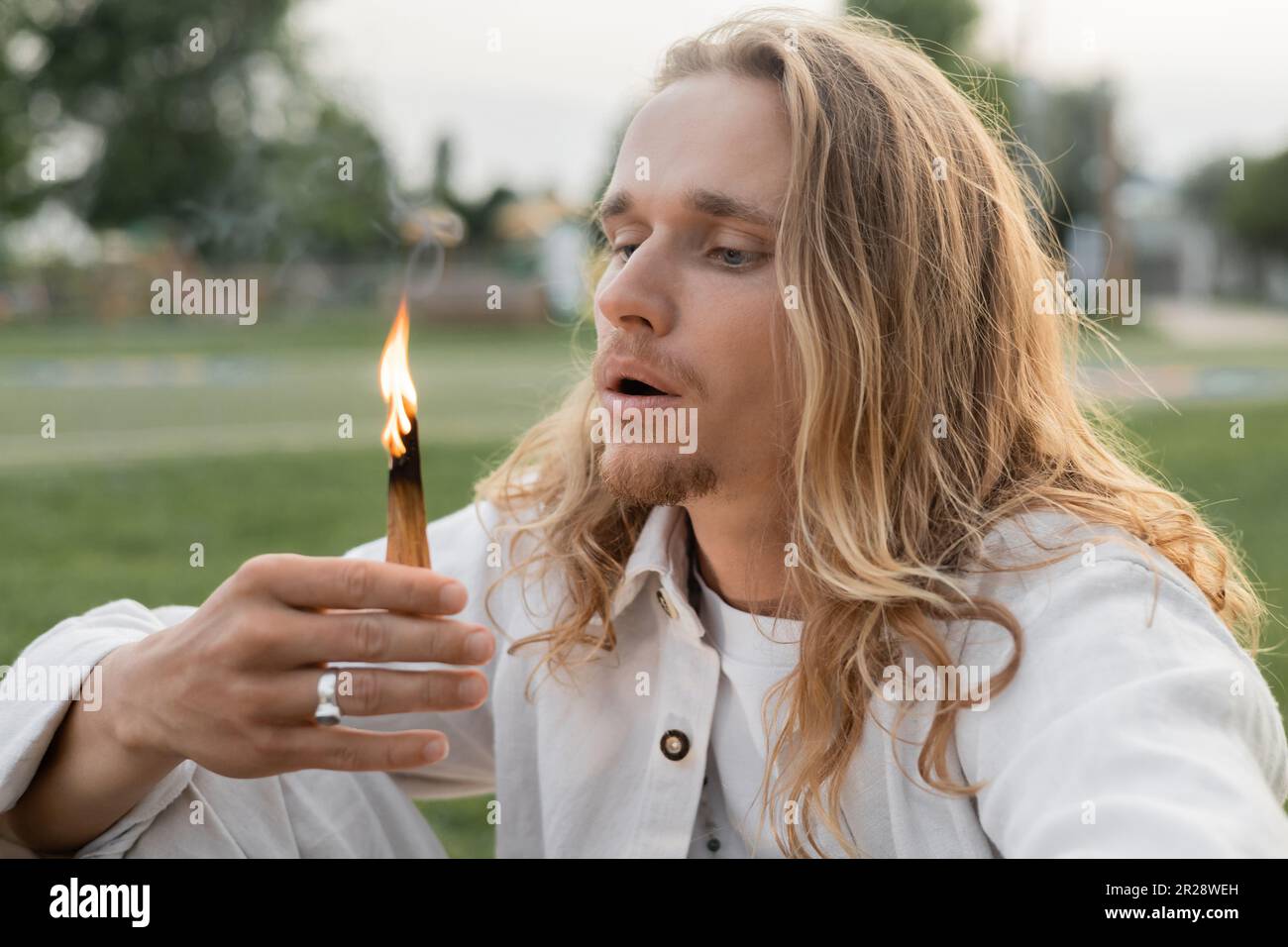 long haired man in white clothes blowing at burning palo santo stick Stock Photo