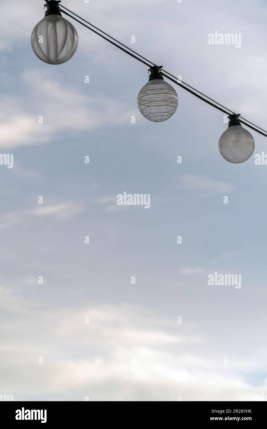 Three light bulbs on string wire against cloudy sky background Stock Photo