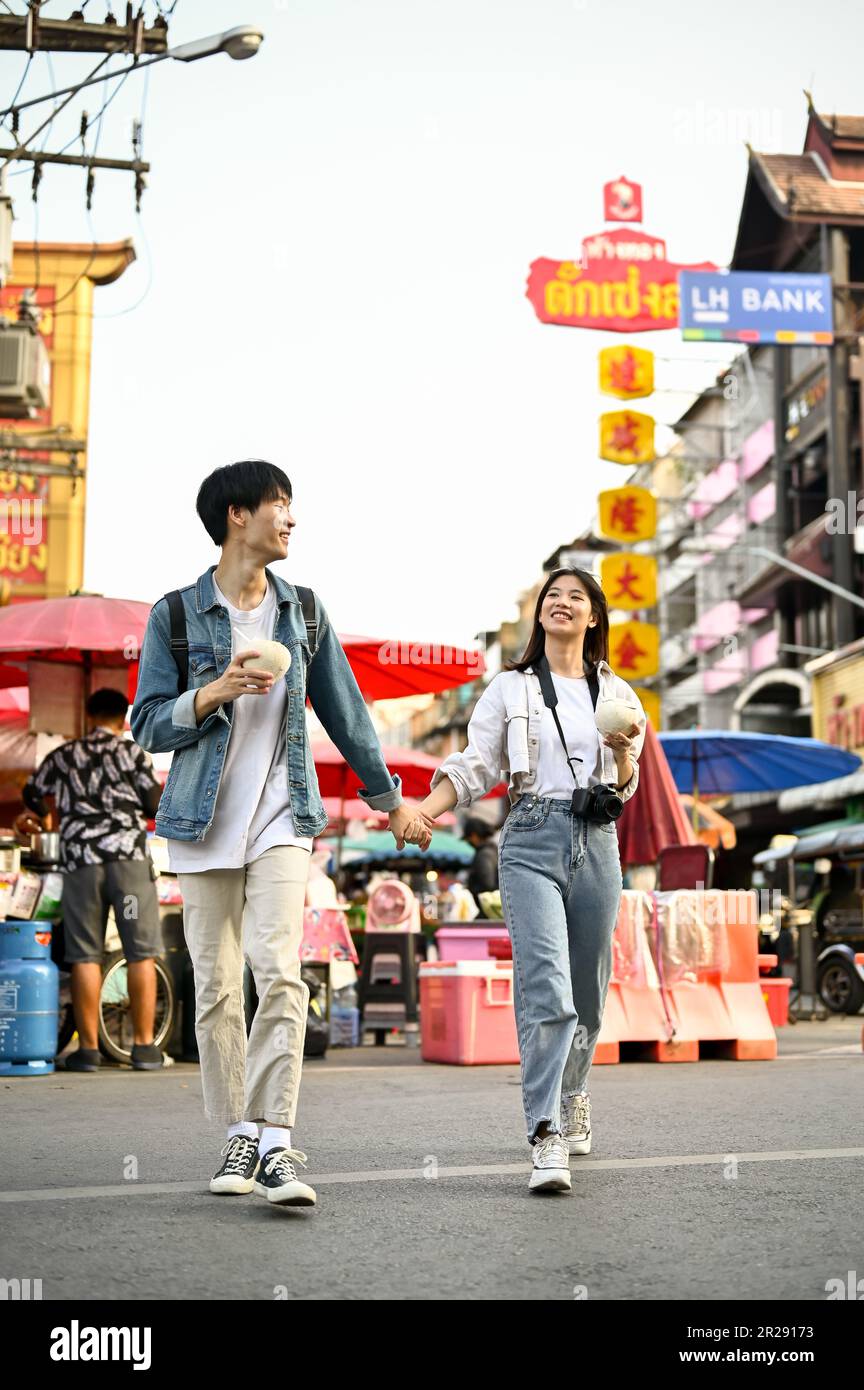 Chiang Mai, Thailand - May 17 2023: Lovely young Asian tourist couple holding hands enjoys walking around Chiang Mai's Chinatown street together. Stock Photo
