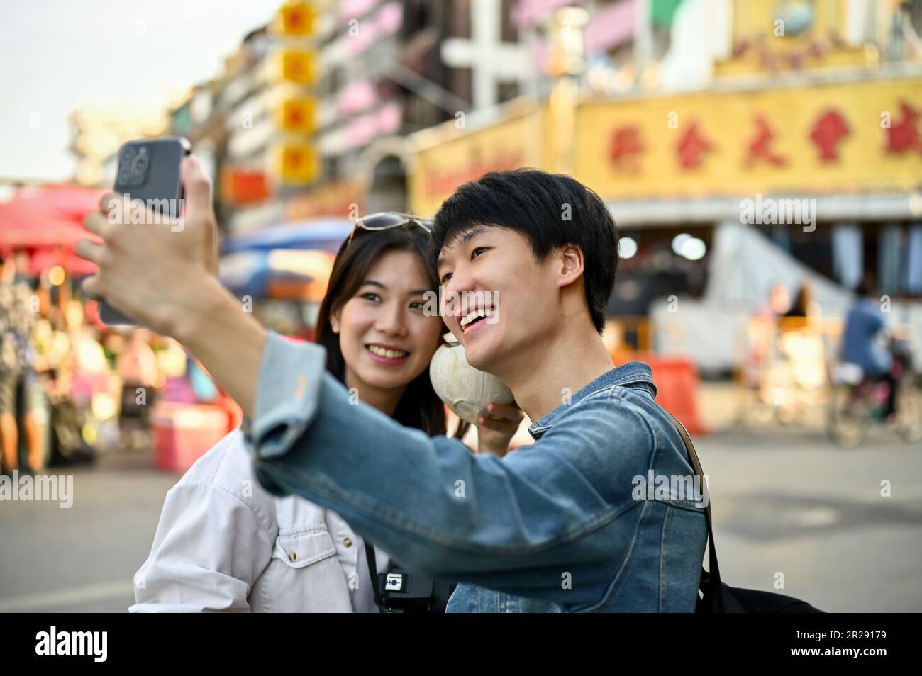 Chiang Mai, Thailand - May 17 2023: Lovely and happy young Asian tourist couple taking a photo with a smartphone in a Chinatown. South East Asia vacat Stock Photo