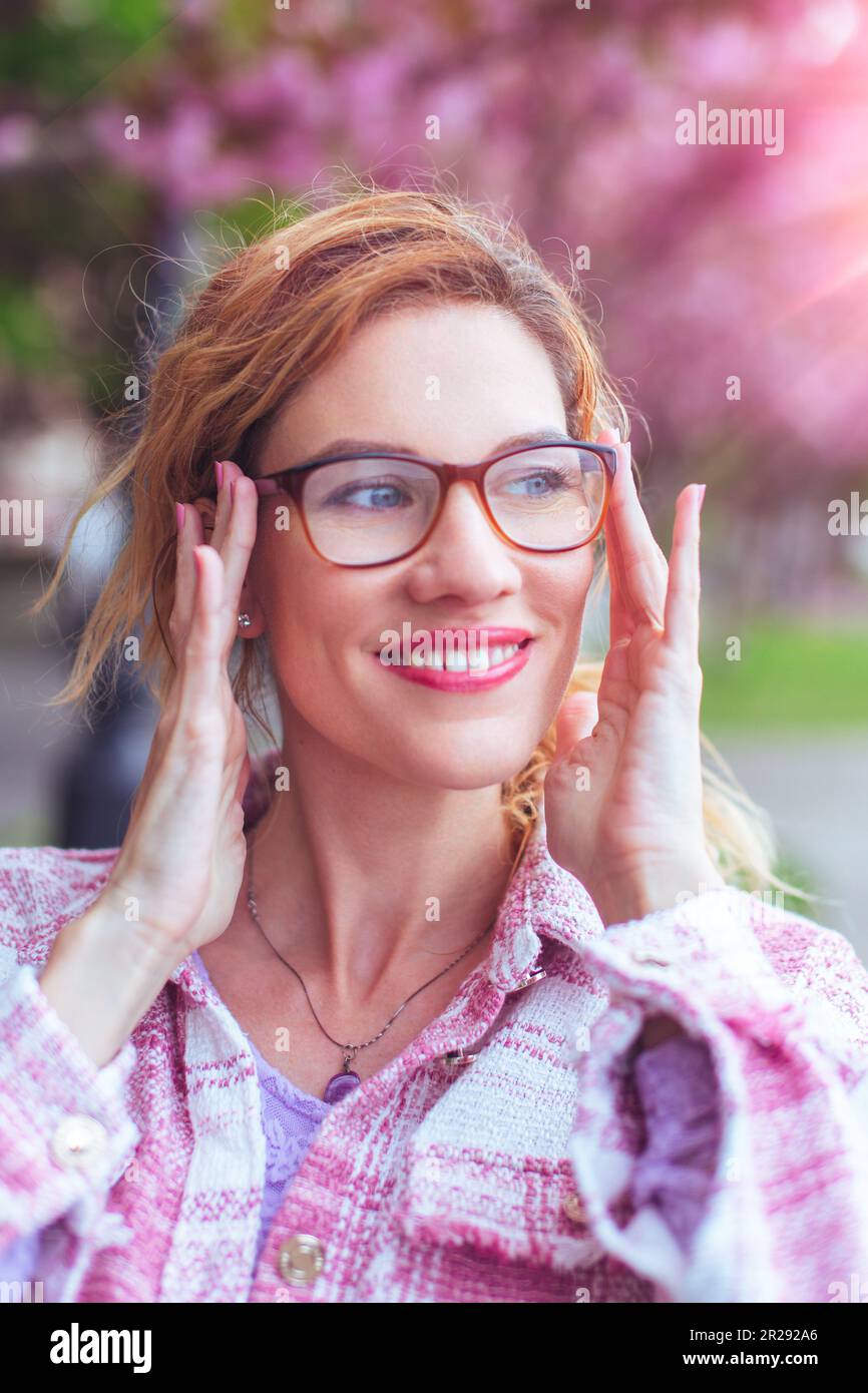 Positive Caucasian woman put on eyeglasses to see clearly outdoors Stock Photo