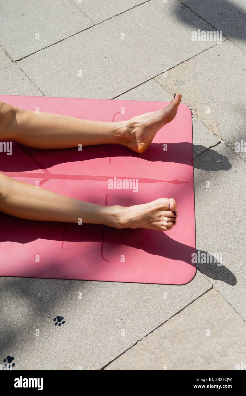 Cropped view of barefoot woman getting tan and lying on yoga mat on urban street, summer concept Stock Photo