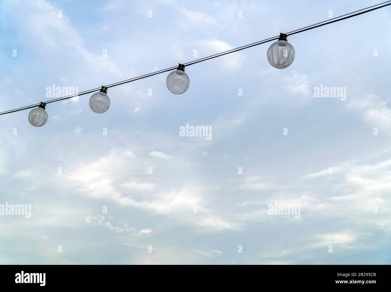 Light bulbs on string wire against cloudy sky background Stock Photo