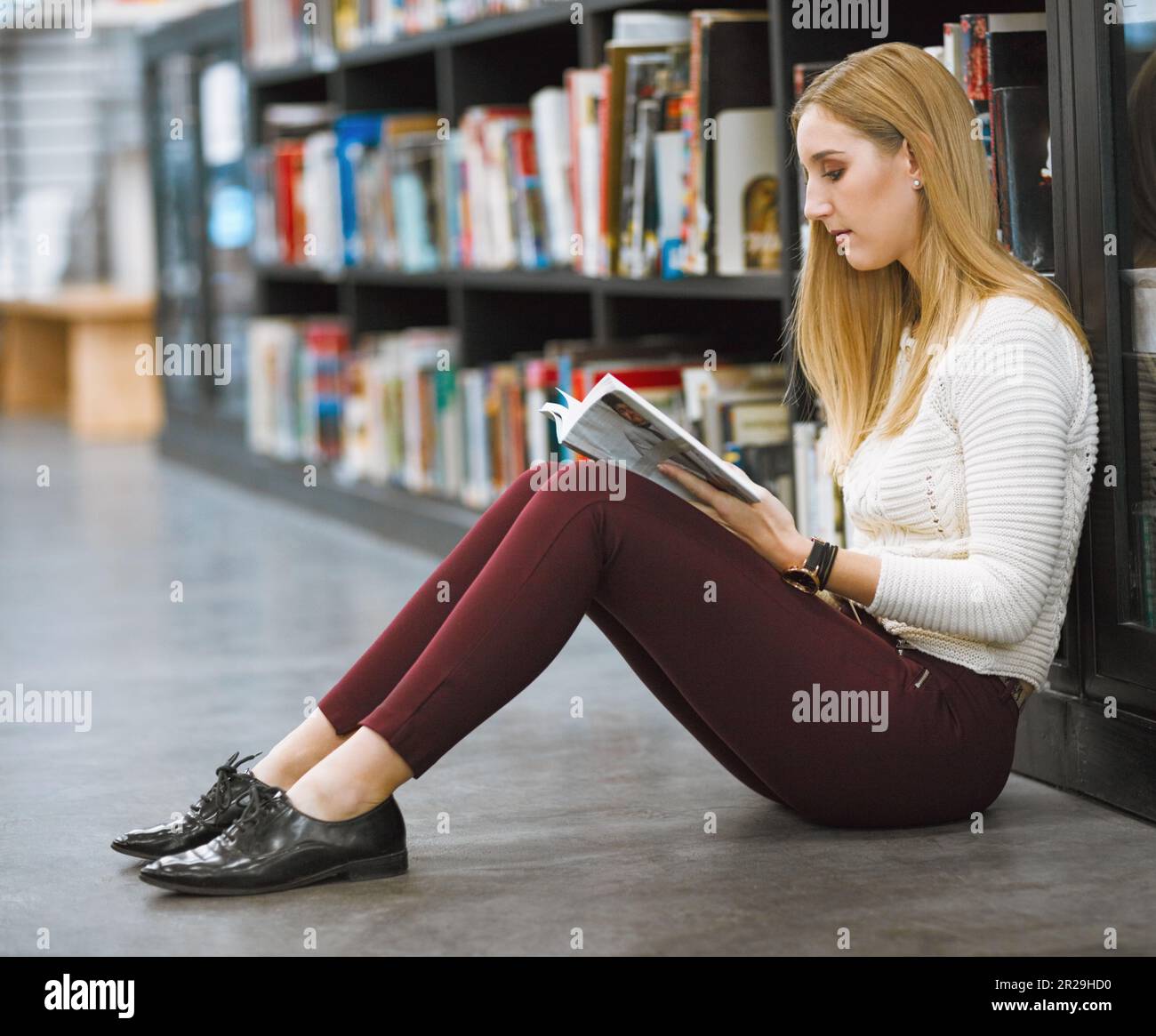 University, student and reading magazine in the library floor or free time studying or information and knowledge in college. Research, learning and Stock Photo