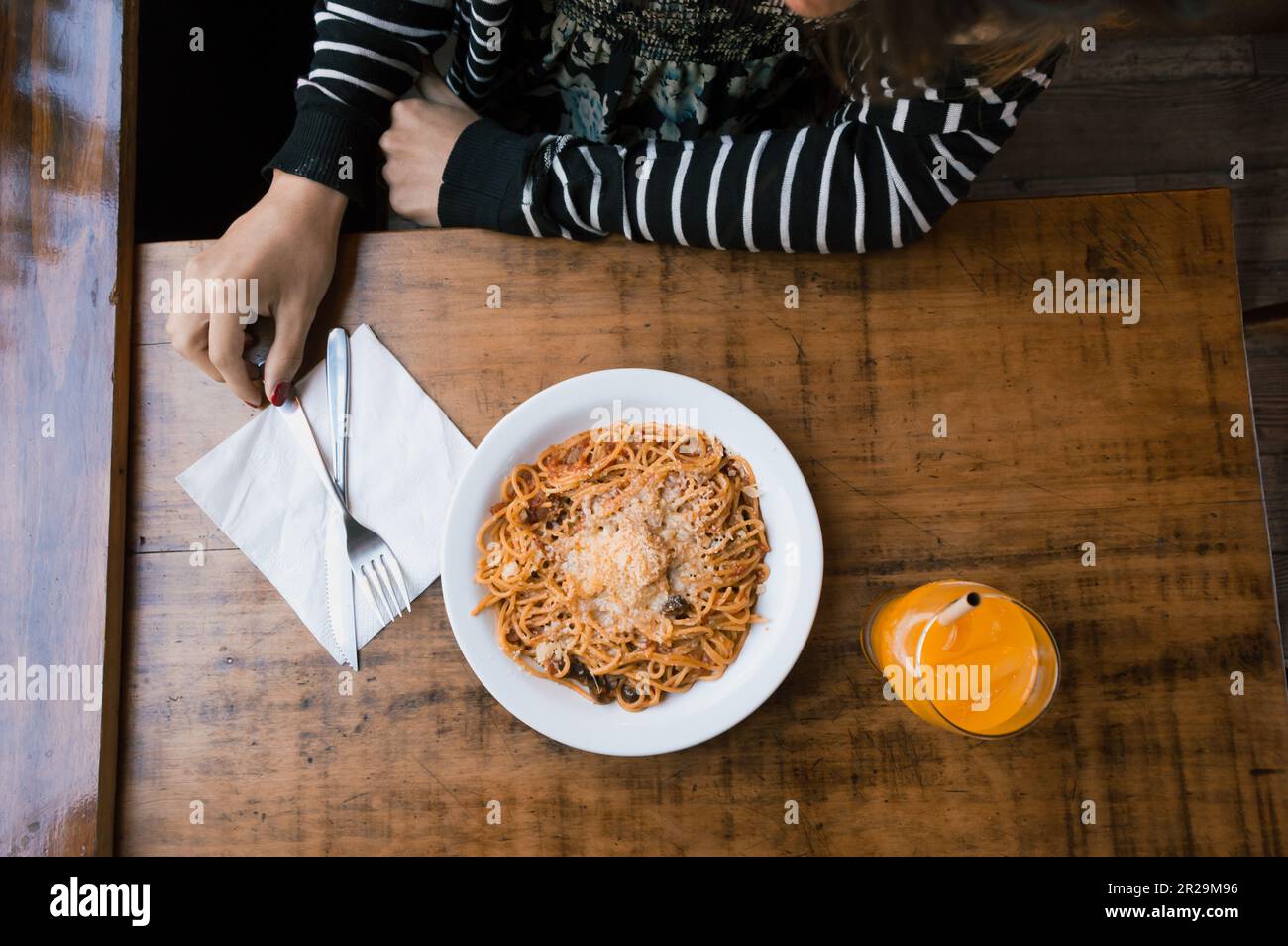 top view of unrecognizable person's arm on a table about to start eating a plate of spaghetti and an orange juice, restaurant concept, copy space. Stock Photo
