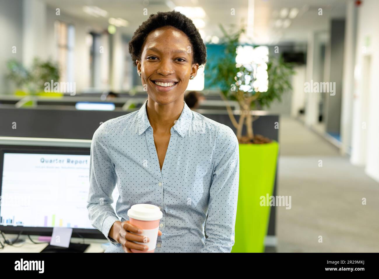 Portrait of smiling african american female architect holding coffee cup sitting in office Stock Photo