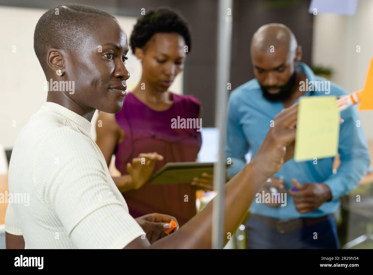 African american woman writing on adhesive note over glass wall while ...
