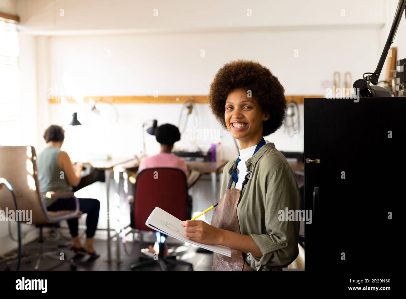 Portrait of happy biracial female worker drawing sketches and smiling at jewellery workshop Stock Photo