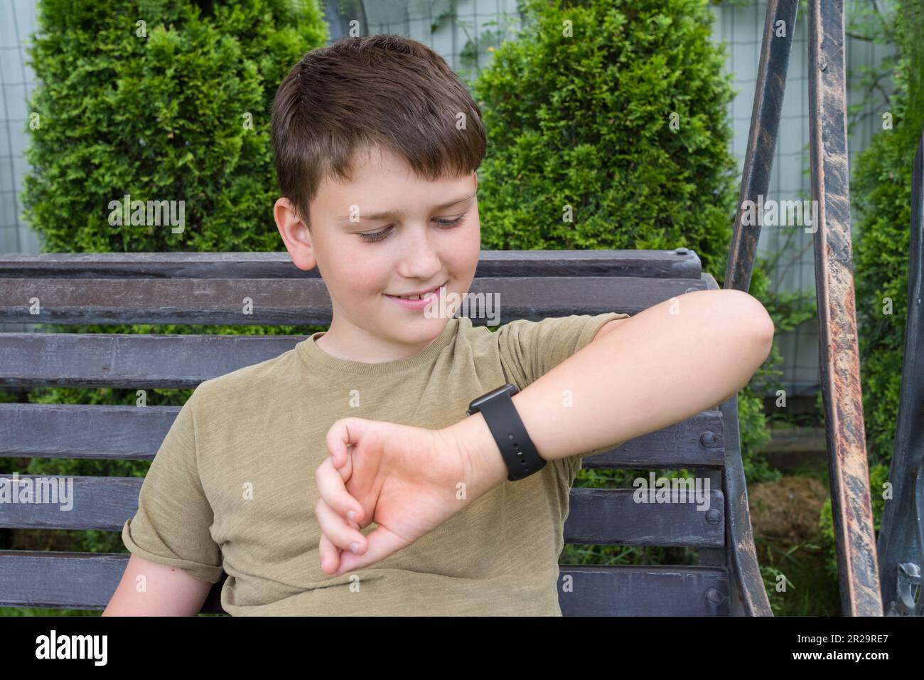 A teenage boy sitting on a bench looking at his watch. The boy in the ...