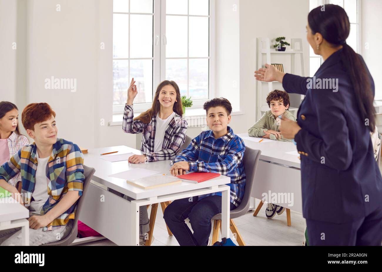 Schoolgirl sitting at the desk raising her hand up ready to answer in ...