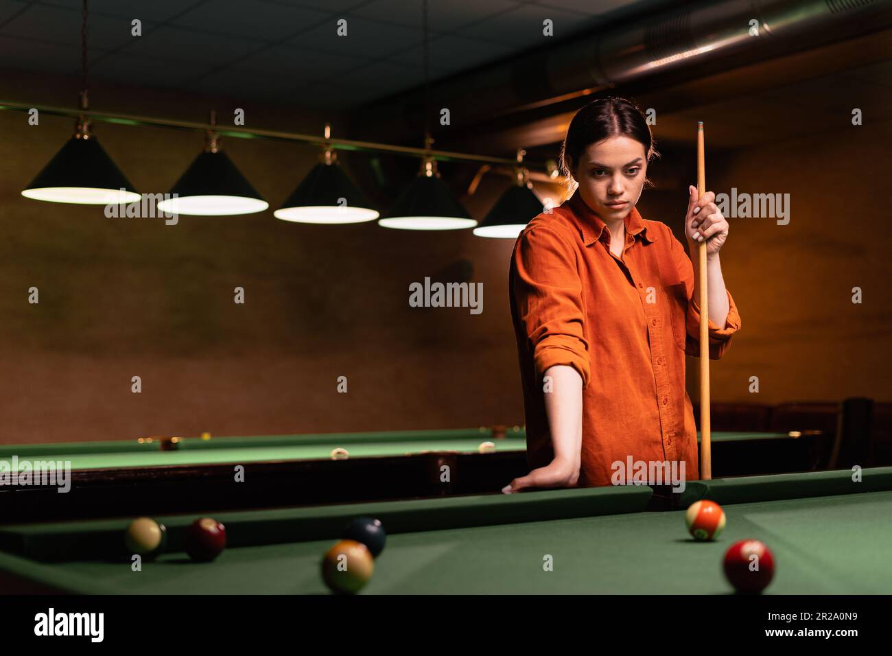 Beautiful girl playing billiards, learning to play billiards. Dark