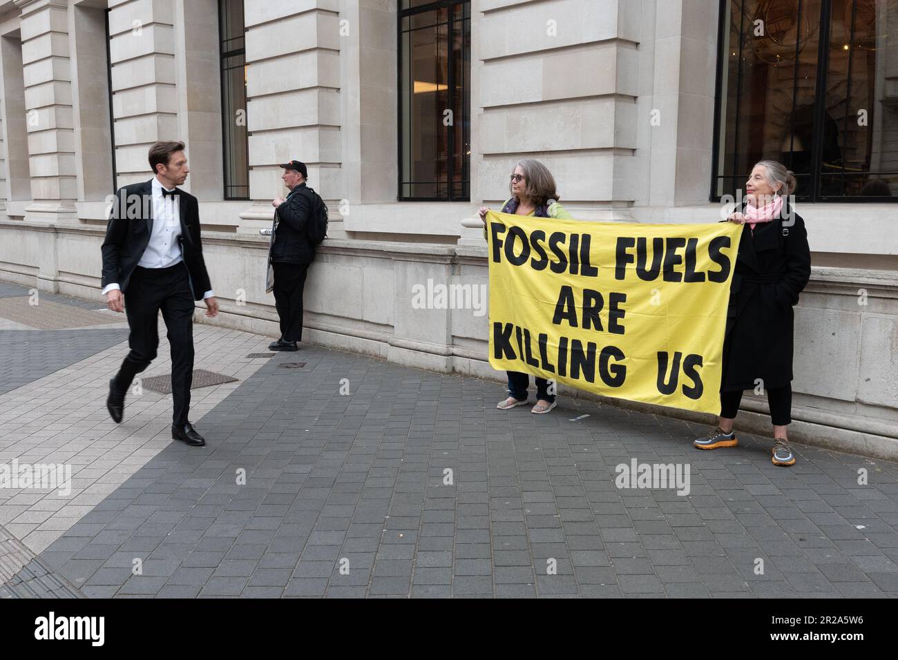 A guest of the Science Museum Director's Annual Dinner walks past climate activists protesting against fossil fuel sponsorship of the Museum. Stock Photo