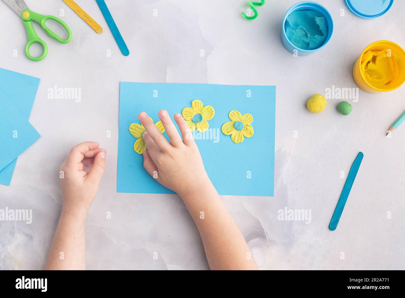 Blue and yellow flowers from plasticine. Kid's craft. Child's hands with dough clay. Colorful clay Stock Photo