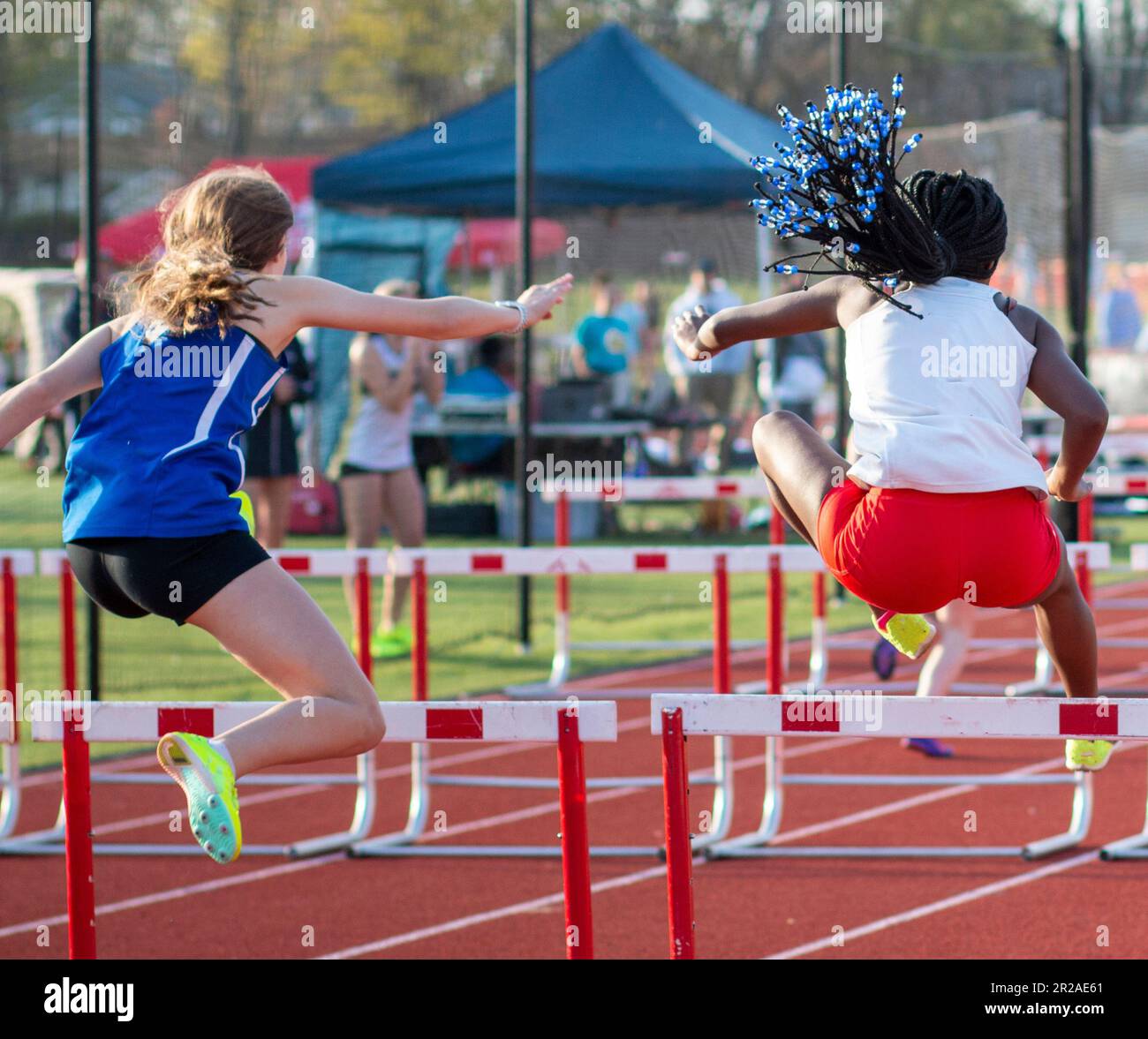 Rear view of two high school girls running in a hurdle race suring a