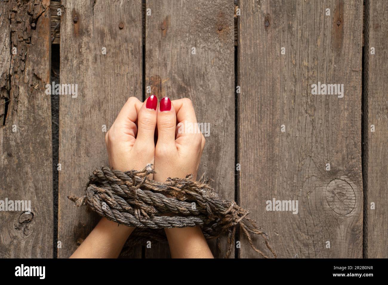 tied female hands with rope on wooden background close up Stock Photo