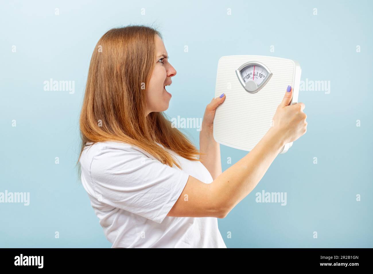 https://c8.alamy.com/comp/2R2B1GN/young-brunette-woman-looking-at-weight-scale-in-shock-on-blue-background-2R2B1GN.jpg