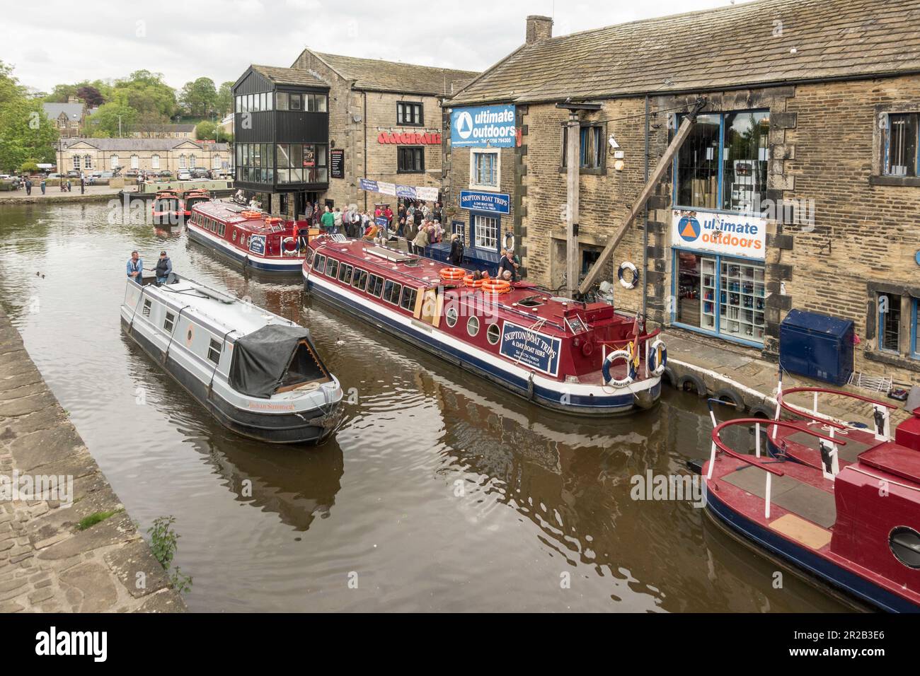 A  canal narrow boat passes people queuing for a boat trip in Skipton, North Yorkshire, England, UK Stock Photo