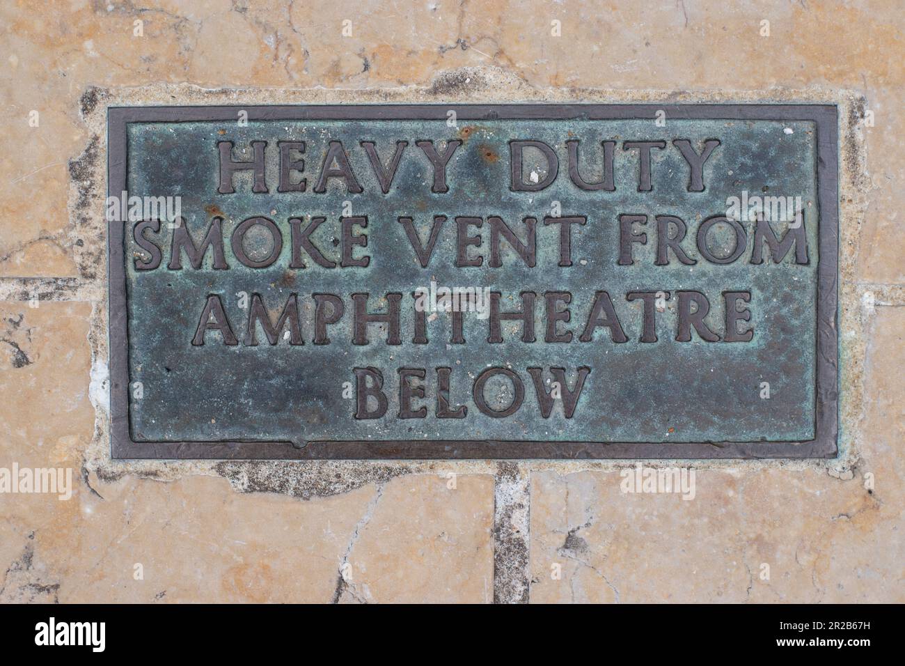 Heavy duty smoke vent from amphitheatre below bronze sign bronze plaque on pavement sidewalk footpath in City of London Stock Photo
