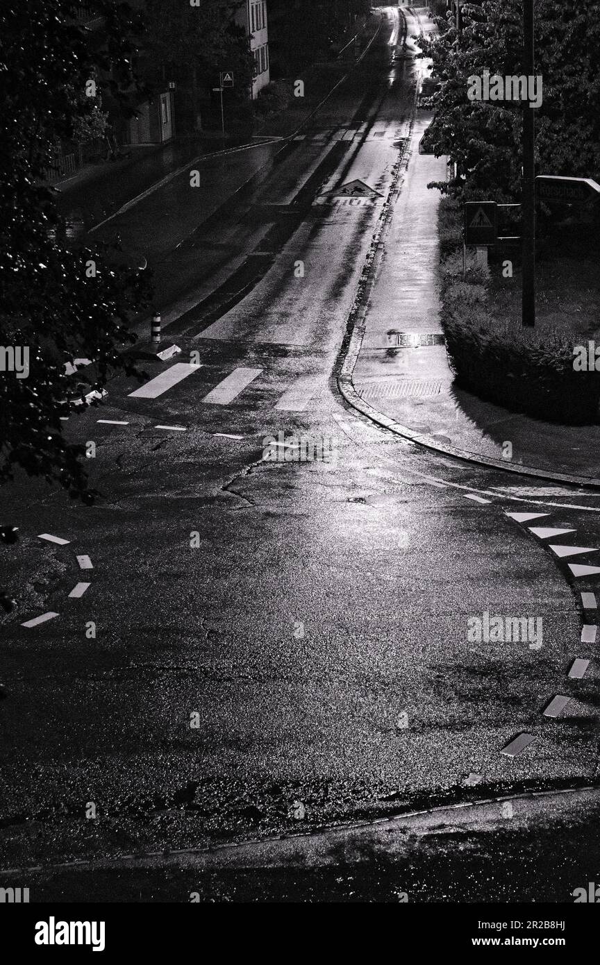 In the silent embrace of the night, a solitary car traverses the dimly lit street. Its headlights cast an ethereal glow, painting the surroundings. Stock Photo