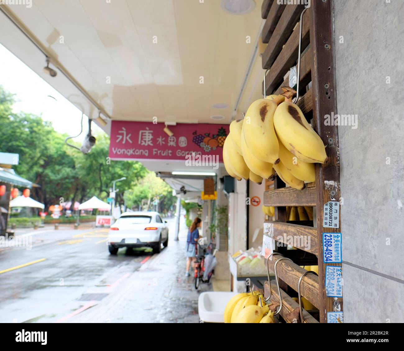 Ripe bananas hanging outside the Yong Kang Fruit Garden store selling fruits and vegetables on Yongkang Street; Da'an District, Taipei, Taiwan. Stock Photo
