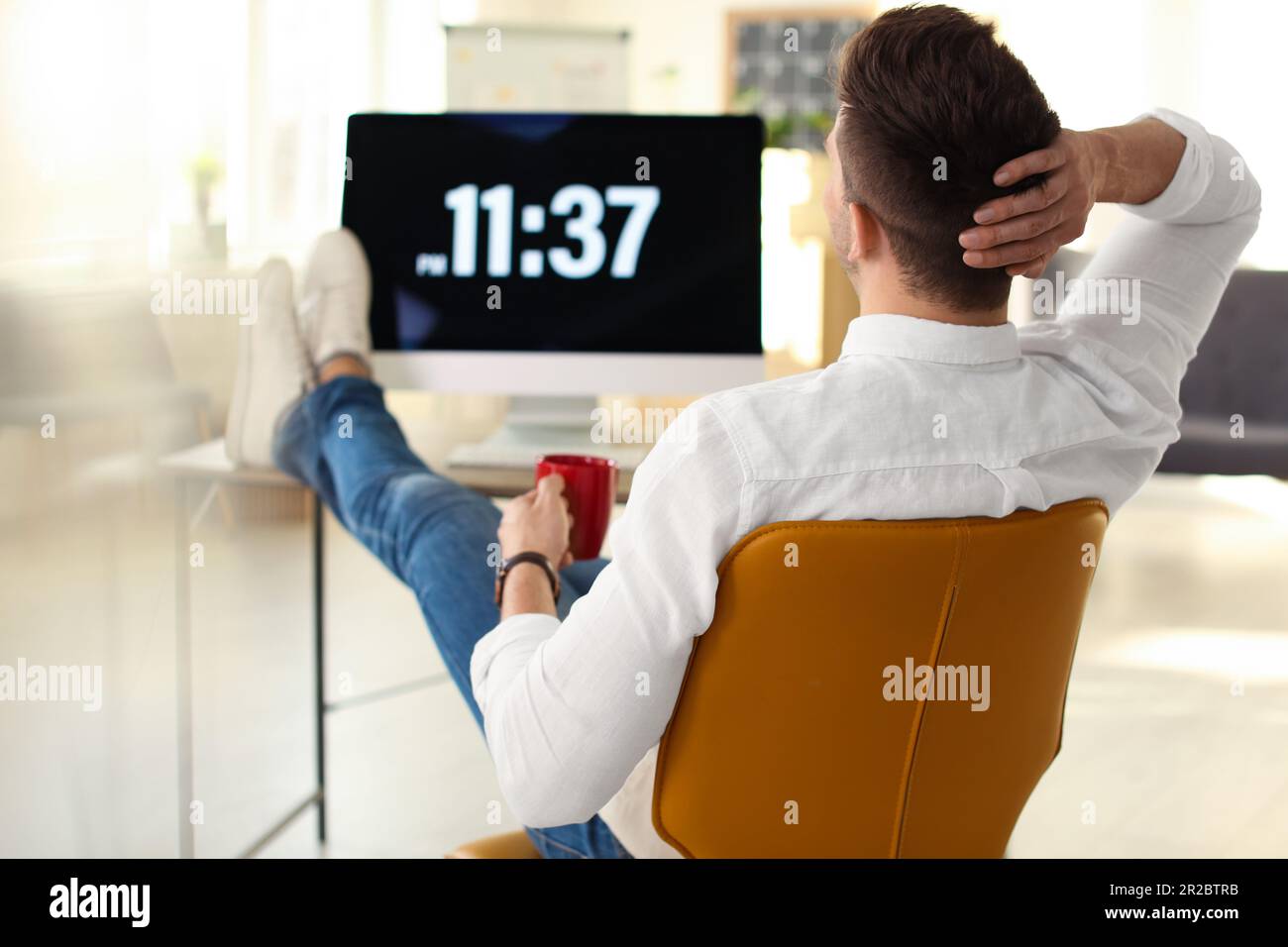 Young businessman with cup of drink relaxing at table in office during break Stock Photo