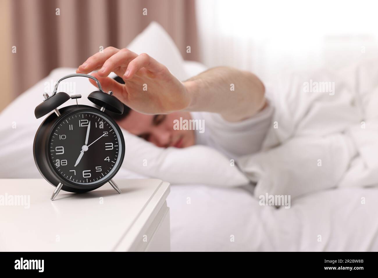 Man turning off alarm clock in bedroom, focus on hand. Space for text