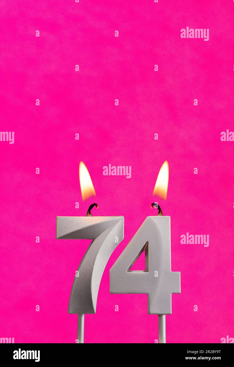 Candle 74 with flame - Silver anniversary candle on a fuchsia background Stock Photo