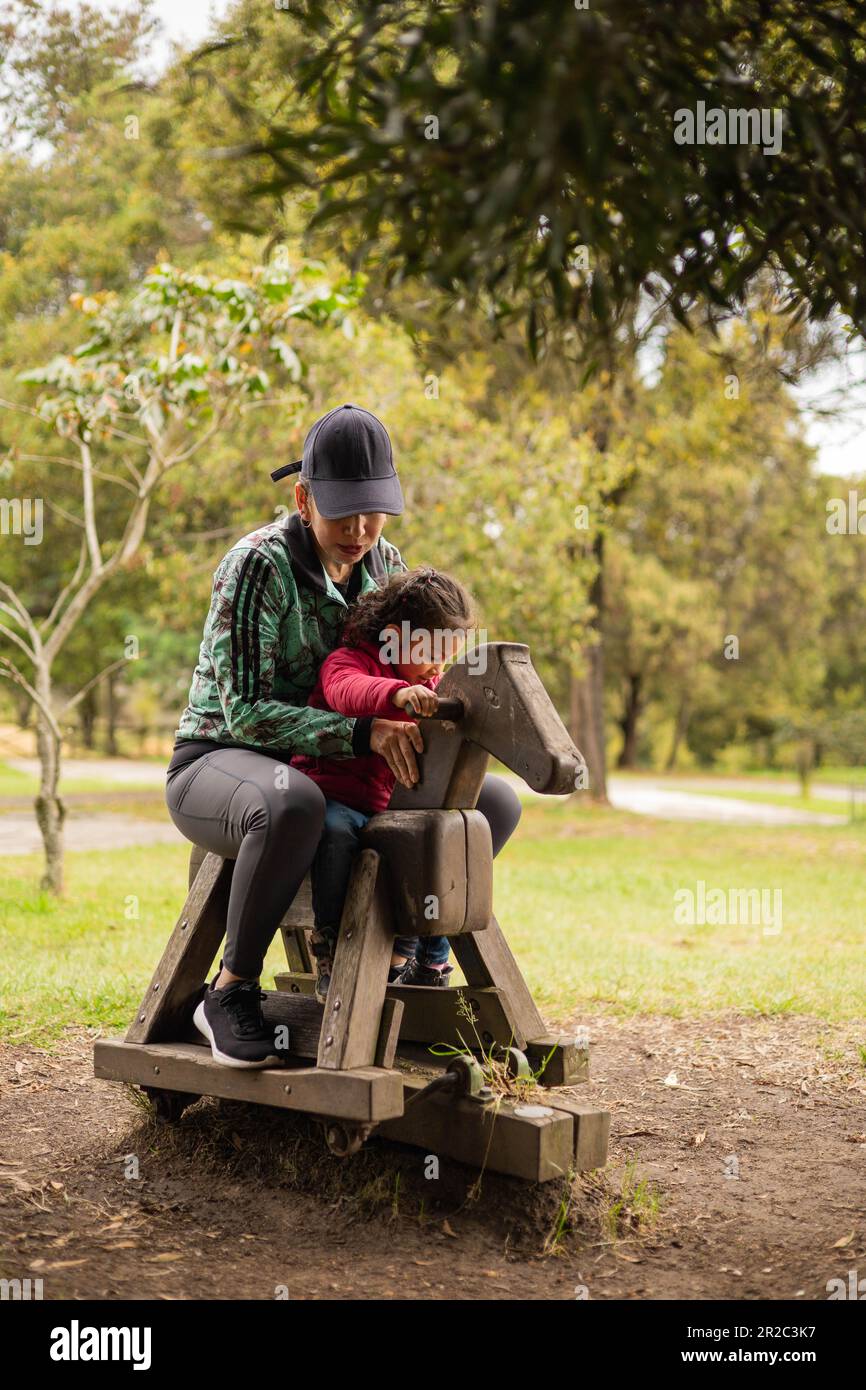 playing on wooden rocking horse shaped, rustic games and playground decoration, mother and daughter enjoying sunny day, family day lifestyle Stock Photo