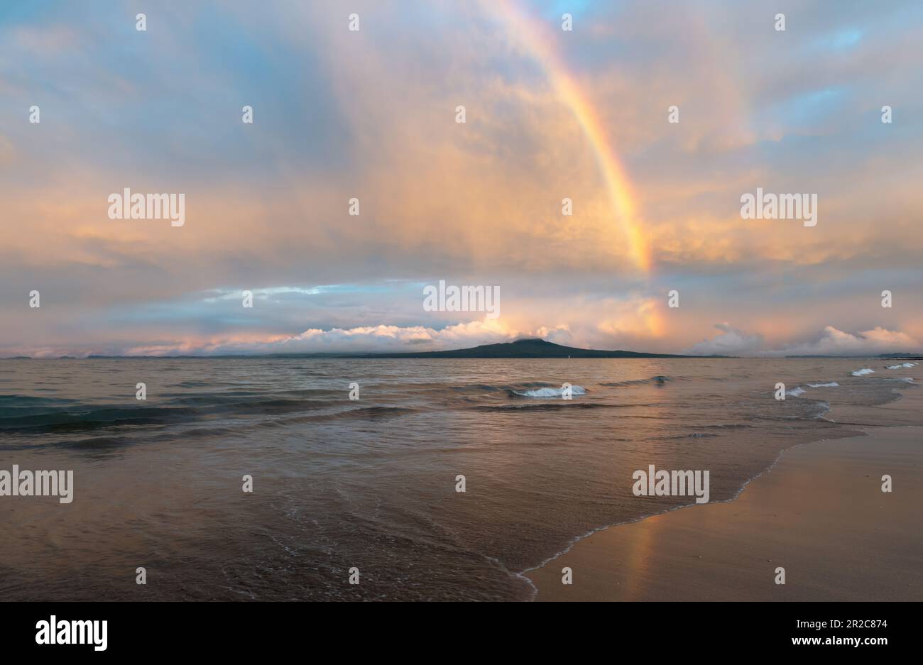Rainbows over Rangitoto Island. Breaking ocean waves on sandy Milford beach. Auckland. Stock Photo