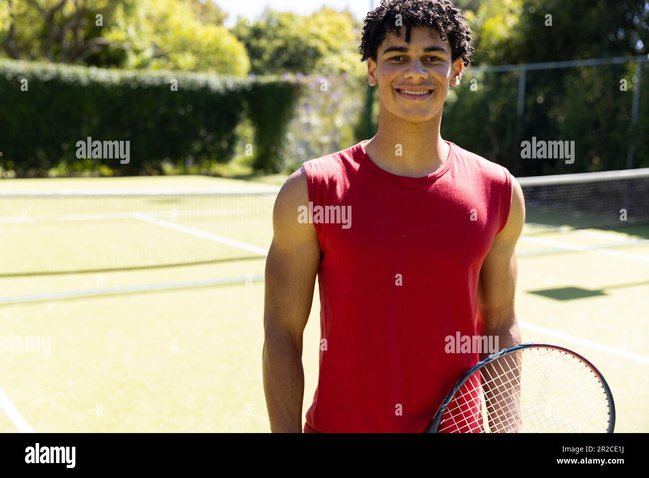 Portrait of smiling biracial fit man with tennis racket on sunny outdoor tennis court Stock Photo