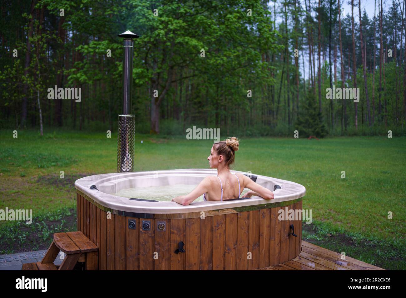 Young happy woman relaxing in hot tub. Enjoying welness SPA outside in the forests. Hot bath SPA Stock Photo
