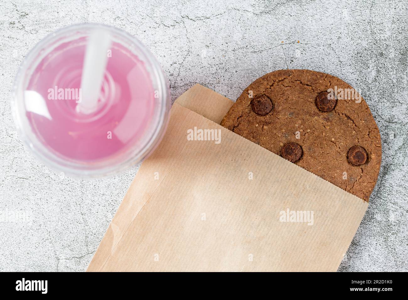 Chocolate chip cookie wrapped in paper bag with drink next to it on stone table Stock Photo