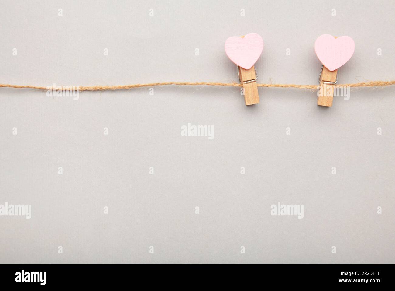 Two pink clothespins hearts hanging on rope on grey background. Top view. Stock Photo
