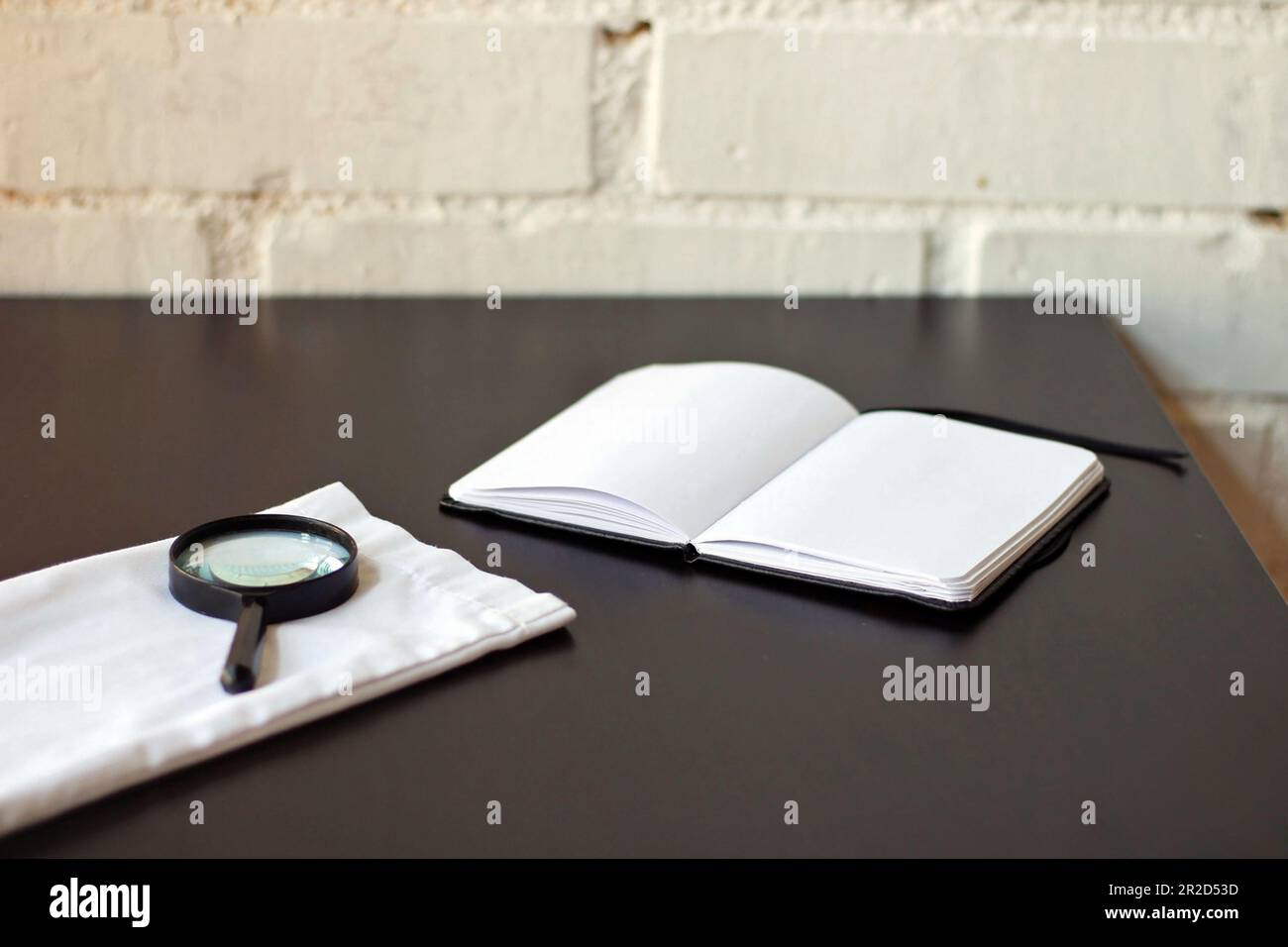 Magnifying glass next to a black notebook Stock Photo - Alamy