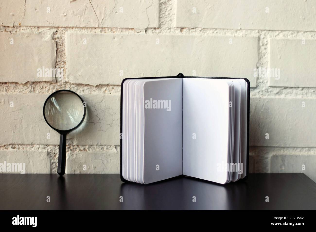 Magnifying glass next to a black notebook Stock Photo - Alamy