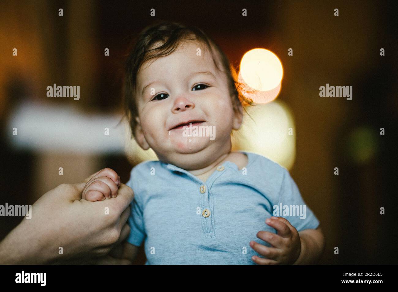 Cute chubby baby smiles and stands with help from parent Stock Photo