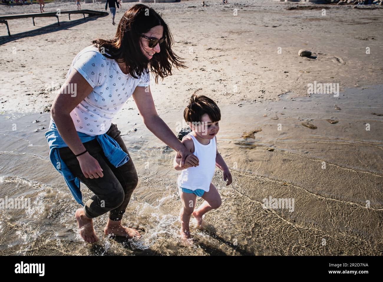 Mother running happy, hand in hand with her little kid on a beach having fun family time. Mom and son enjoy their freedom on vacation by the sea Stock Photo