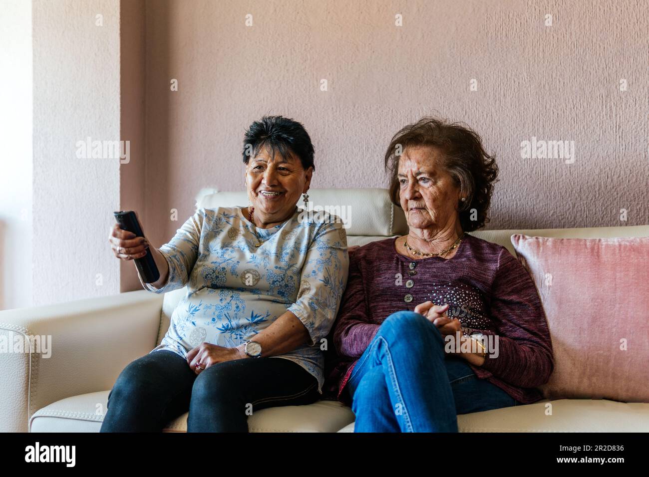 two older modern women watching tv sitting on the sofa Stock Photo