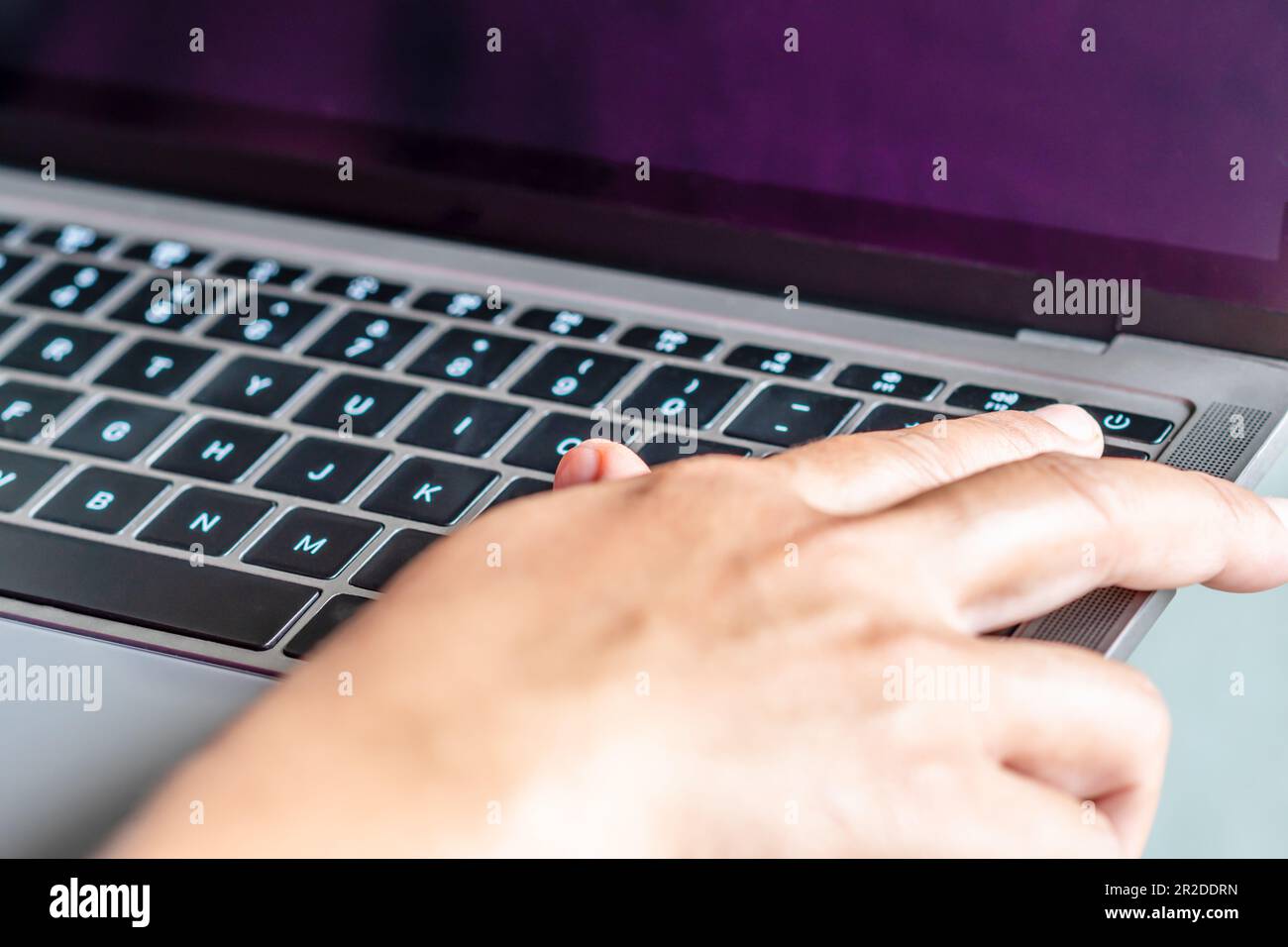 After clicking saving all business work use your finger to press the button to turn it off closed the gray laptop computer, placed it on a table, is t Stock Photo