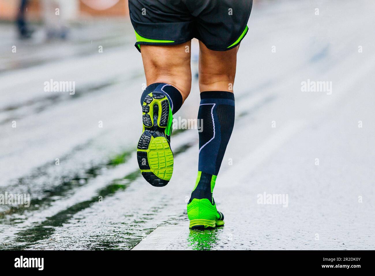 close-up legs runner athlete running marathon in black compression socks, male run on wet asphalt Stock Photo