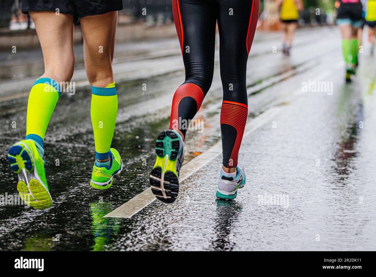 legs female runners running together marathon on wet asphalt, green