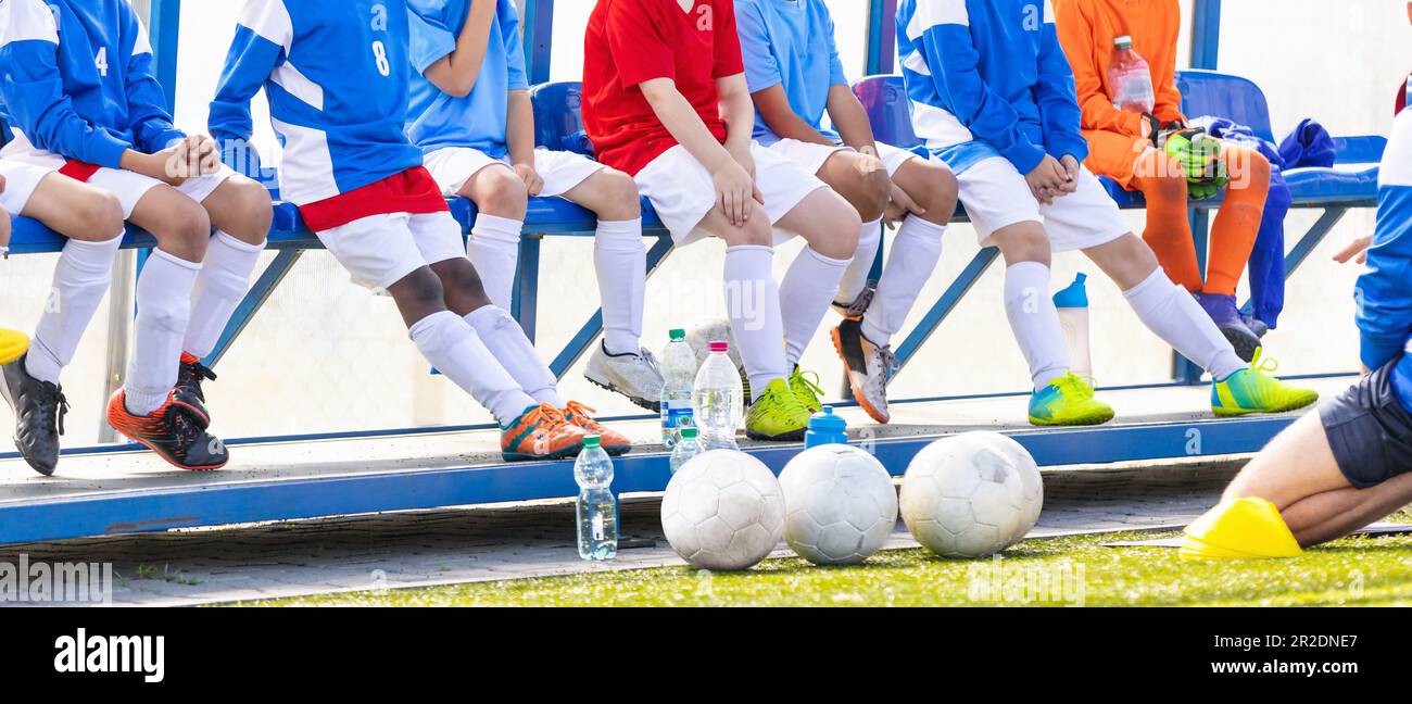 School boys litening to soccer coach during time break at football tournament. Football soccer match for children. Kids waiting on a bench Stock Photo