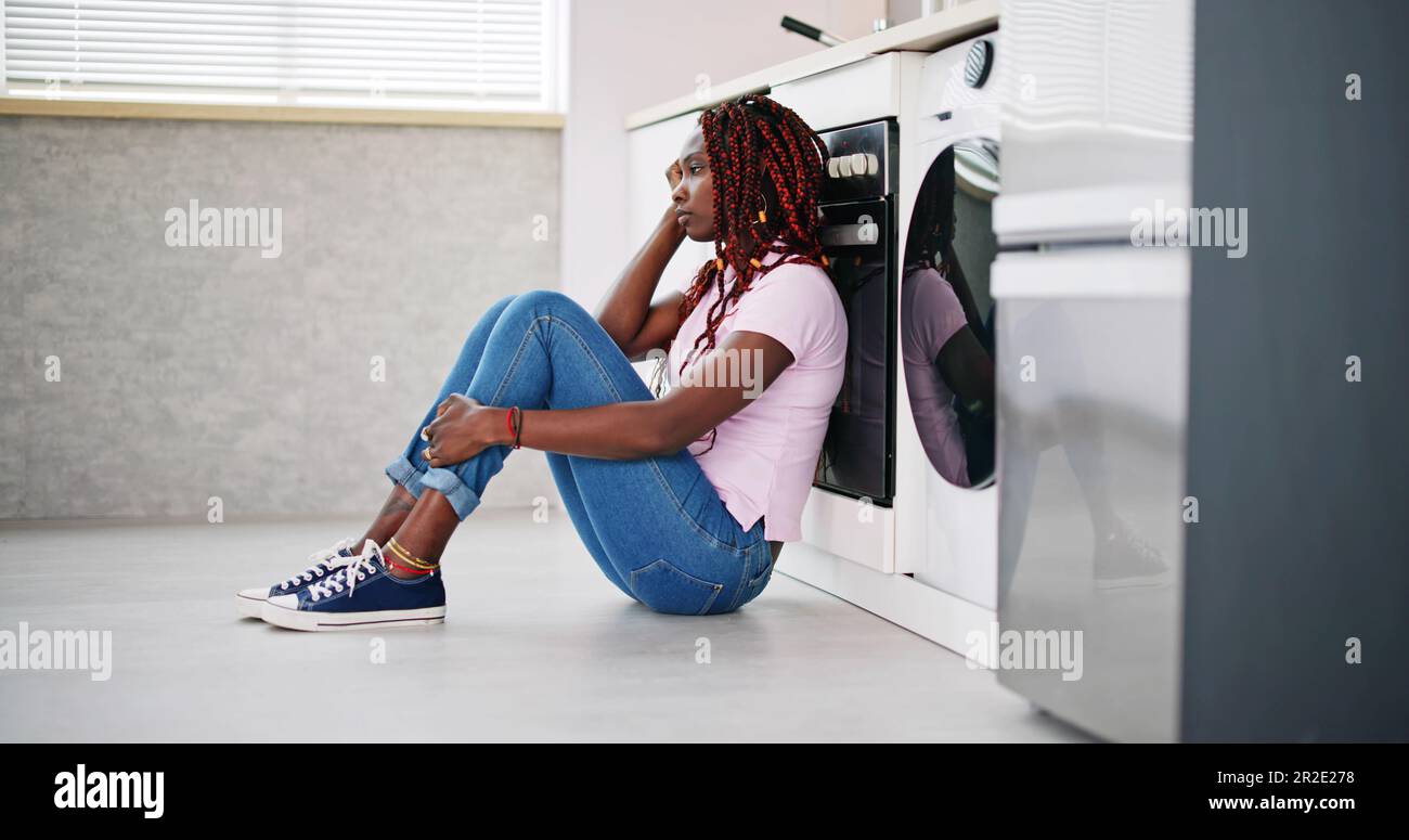 Frustrated Young Woman Sitting On Kitchen Floor Stock Photo