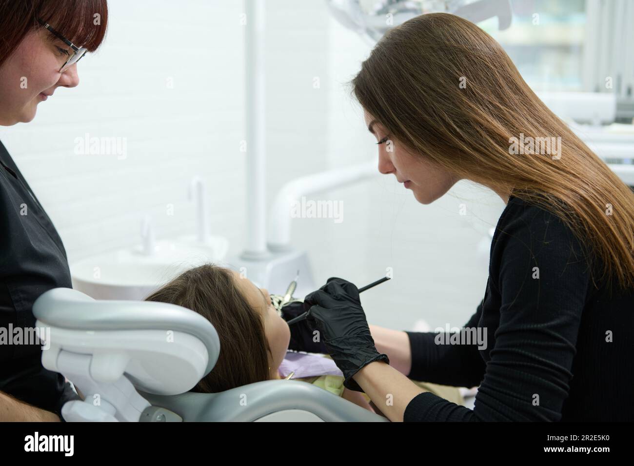 Female dentist hygienist using dental mirror and probe, checking child