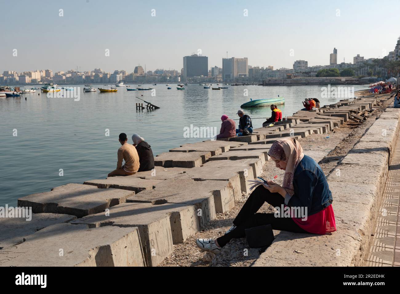 People sit on concrete blocks positioned as a defence against rising sea levels along the Corniche of Alexandria, the seconds largest city in Egypt. Stock Photo