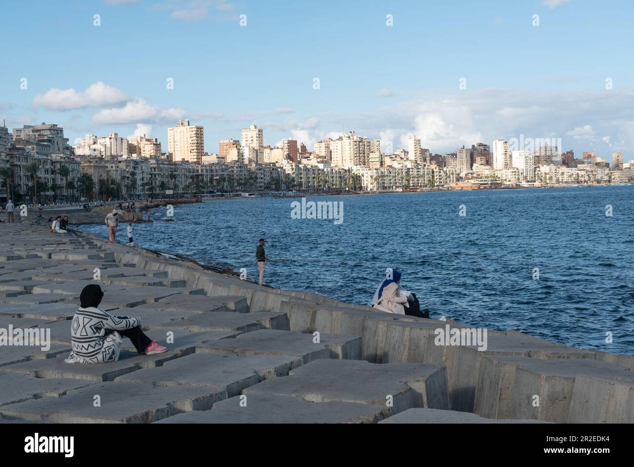 People sit on concrete blocks positioned as a defence against rising Mediterranean sea levels along the Corniche of Alexandria, the seconds largest city in Egypt. Stock Photo